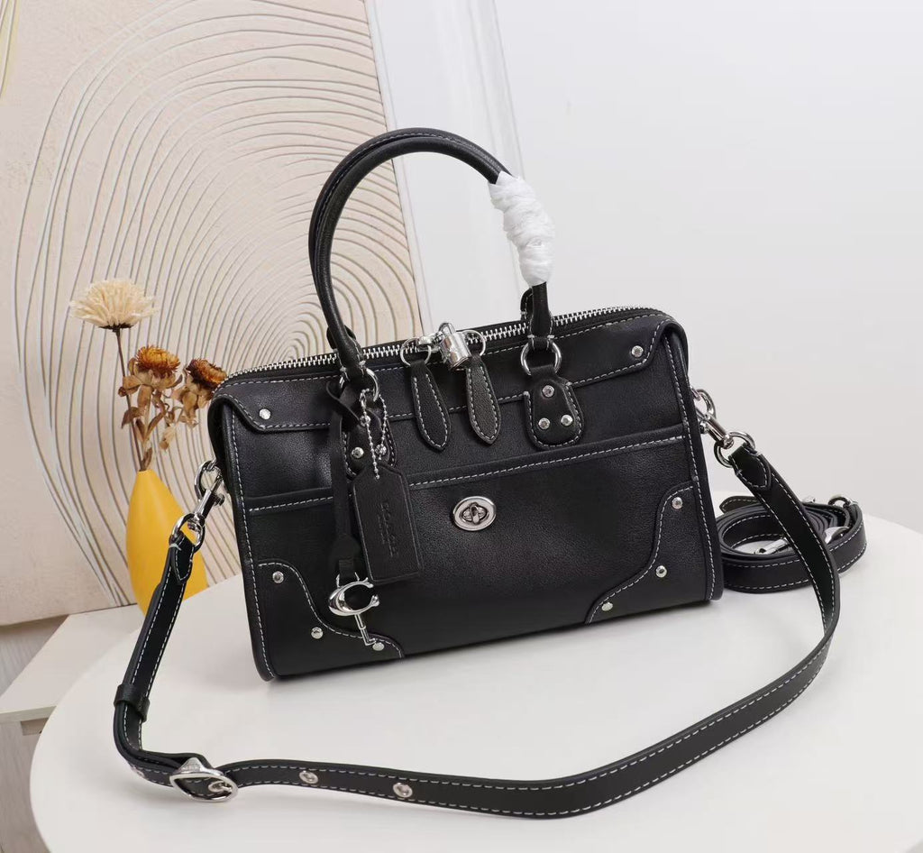 A black leather handbag with silver-tone hardware, a top handle, and a detachable shoulder strap, displayed on a white surface with a decorative background.