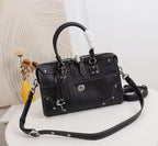 A black leather handbag with silver-tone hardware, a top handle, and a detachable shoulder strap, displayed on a white surface with a decorative background.