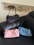 Three Coach handbags in pink, black, and blue are arranged on a black leather sofa with decorative objects on a shelf behind them.