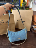 Blue handbag with chain detail held by a hand, with Coach bags and packaging in the background.