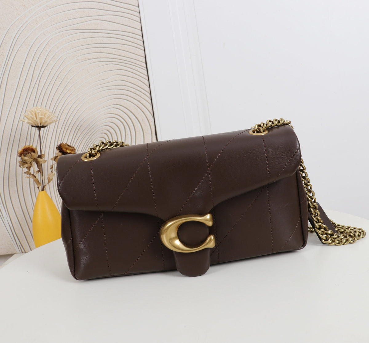 Brown handbag with gold chain and clasp on a white surface with decorative elements.