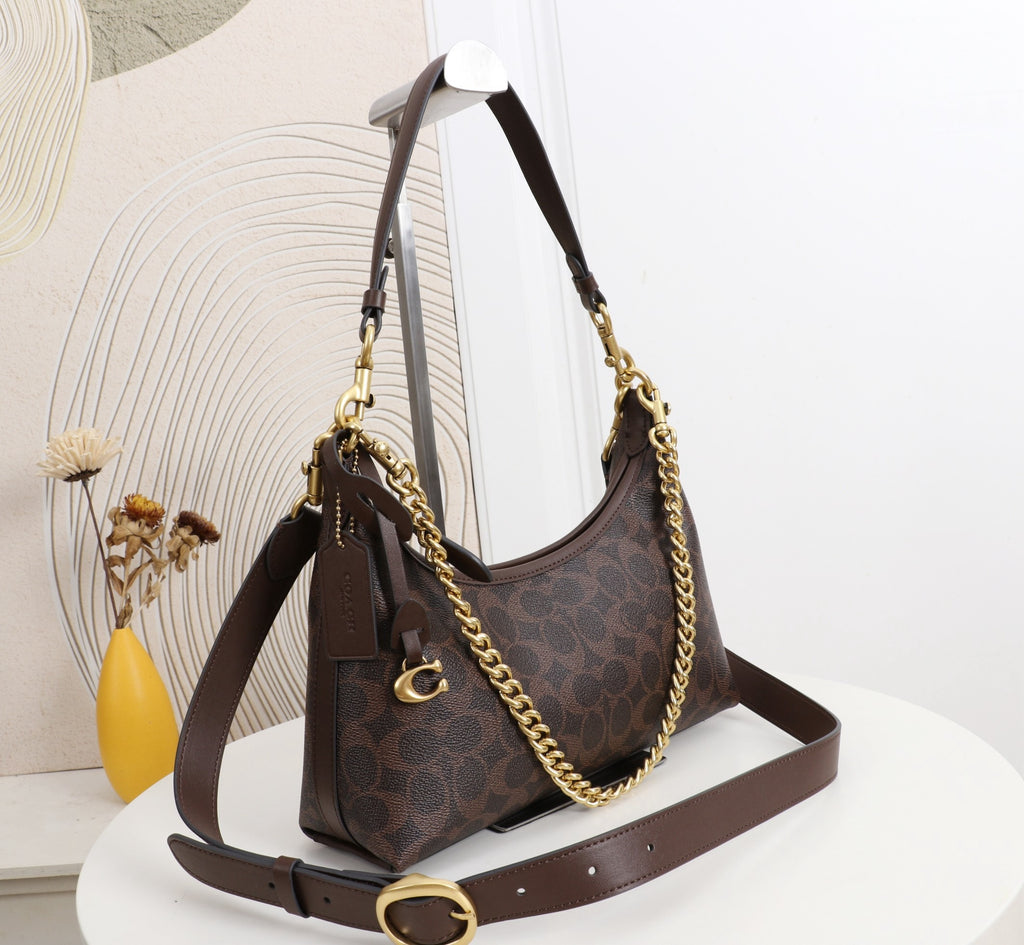 A brown monogram shoulder bag with a gold chain strap and matching brown leather shoulder strap, displayed on a white table against a light background.