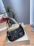 A black shoulder bag with decorative bows, cherries, and gold-tone hardware, held by a hand over an open beige box on a wooden table with a plant in the background.