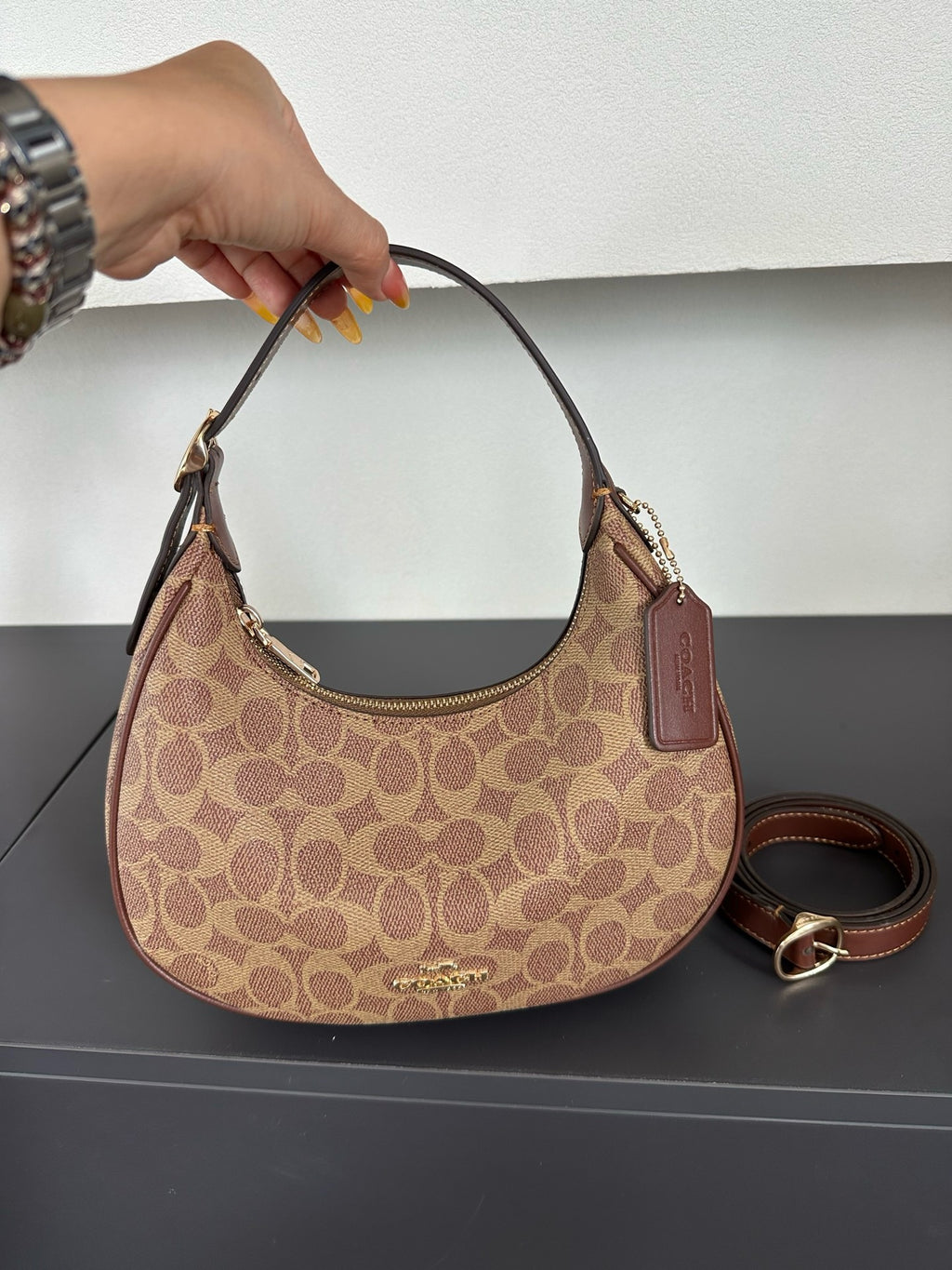 Beige handbag with brown accents held by a hand on a dark surface.