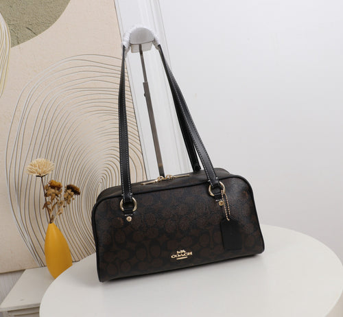 A Coach satchel handbag in their signature dark brown monogram canvas, displayed on a white table with a decorative background.