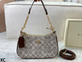 A Coach handbag in the signature monogram canvas, featuring a brown leather top handle, gold-tone chain strap, and a matching brown leather tag. A matching Coach box is visible in the background on a light-colored surface.