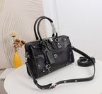 A black leather handbag with silver-tone hardware, dual top handles, a detachable shoulder strap, and a hanging keychain, displayed on a white round table with a decorative background.