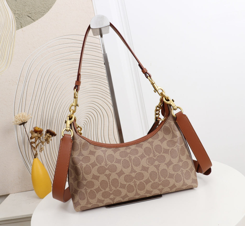 A Coach hobo shoulder bag in the classic monogram canvas, featuring brown leather trim and gold-tone hardware, displayed on a white table with a decorative background.