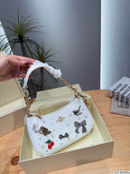 A white Coach handbag with black bow and cherry embellishments, held by a hand over an open cream-colored Coach box on a wooden table.