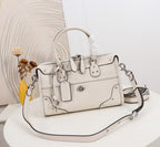 An off-white leather handbag with silver-tone hardware, a top handle, and a detachable shoulder strap, displayed on a white table with a decorative background.