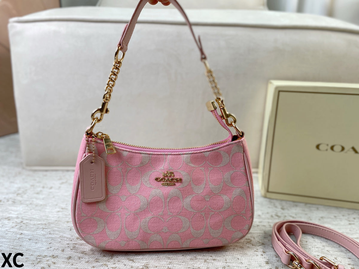 A pink Coach shoulder bag with a signature monogram pattern, gold-tone hardware, and a matching pink leather strap, shown with a Coach box in the background.