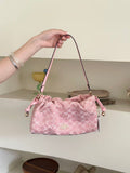 A pink Coach handbag with a signature monogram pattern, held by a person's hand in front of a neutral indoor background.