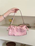 A pink Coach handbag with a signature monogram pattern, held by a person's hand in front of a neutral indoor background.