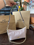 White handbag with gold chain strap held by a hand, with Coach bags in the background.