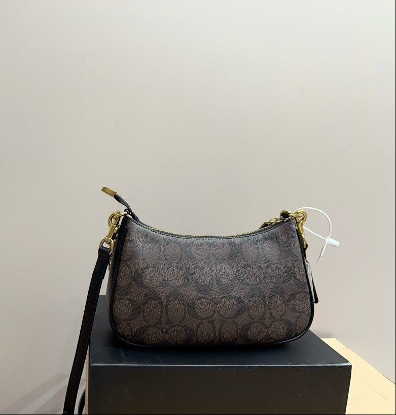 A Coach shoulder bag in the signature monogram canvas, resting on a black display box against a plain light gray wall.