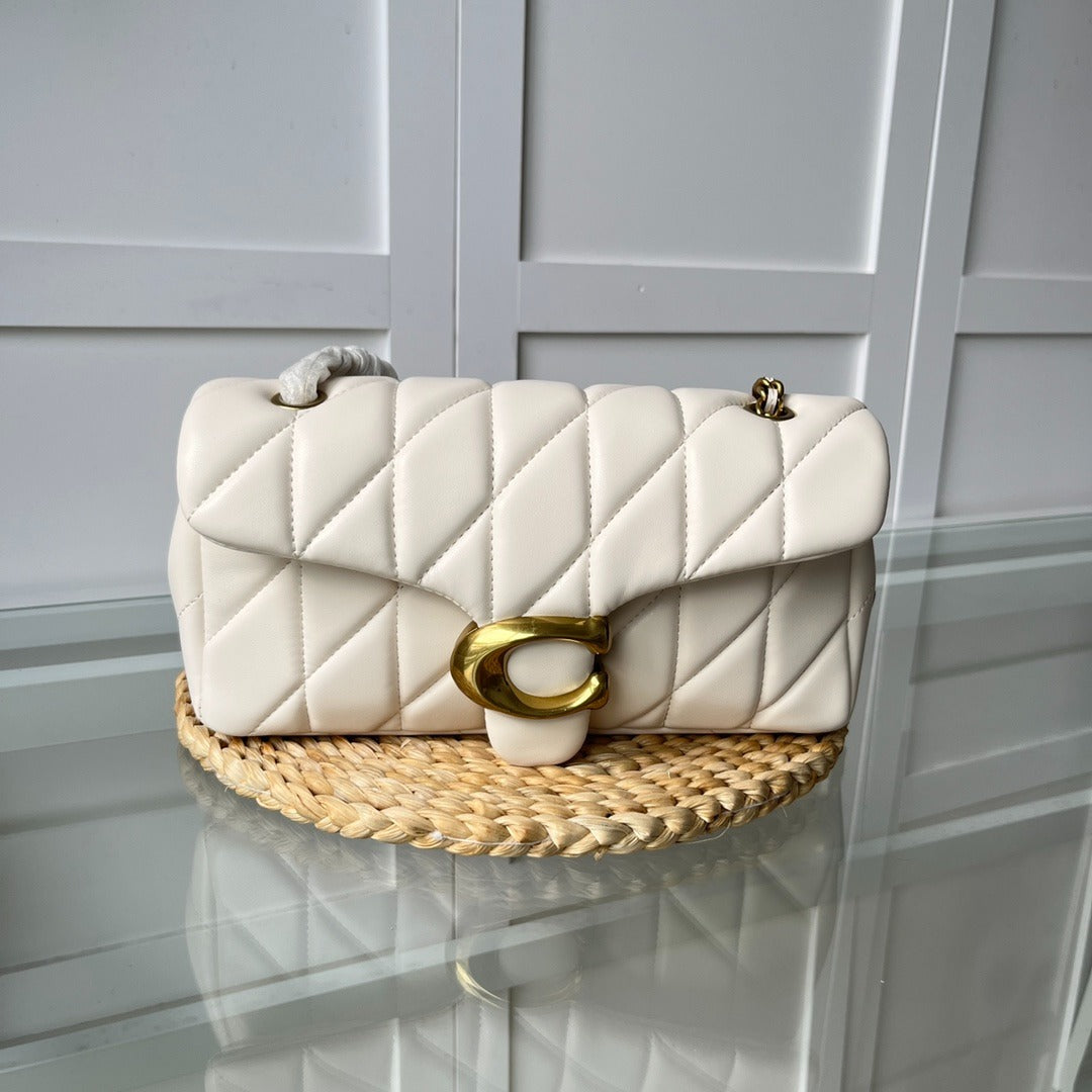 White quilted handbag with gold clasp on a woven mat against a light gray paneled wall.