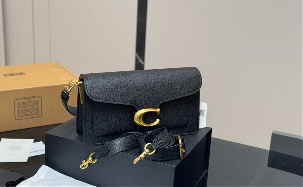 Black handbag with gold accents on a reflective surface next to a cardboard box.