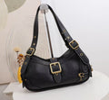 A black pebbled leather shoulder bag with gold-tone hardware, displayed on a stand against a light background with a decorative dried flower prop.
