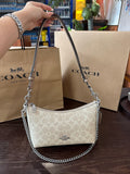 Coach handbag with chain detail held by a hand, with Coach bags and products in the background.