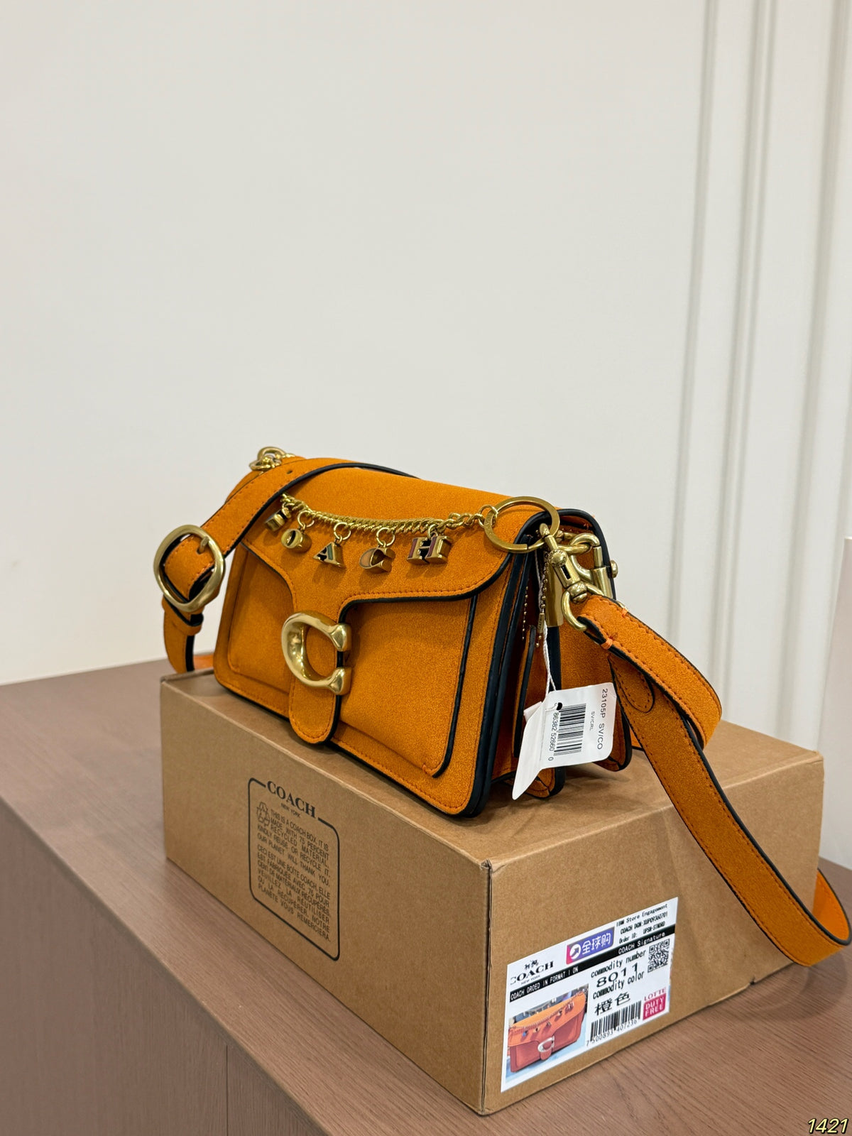 A Coach shoulder bag in mustard yellow suede with gold-tone hardware and horsebit charms, resting on top of a brown cardboard box.