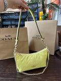 Yellow handbag with chain detail held above Coach shopping bags.