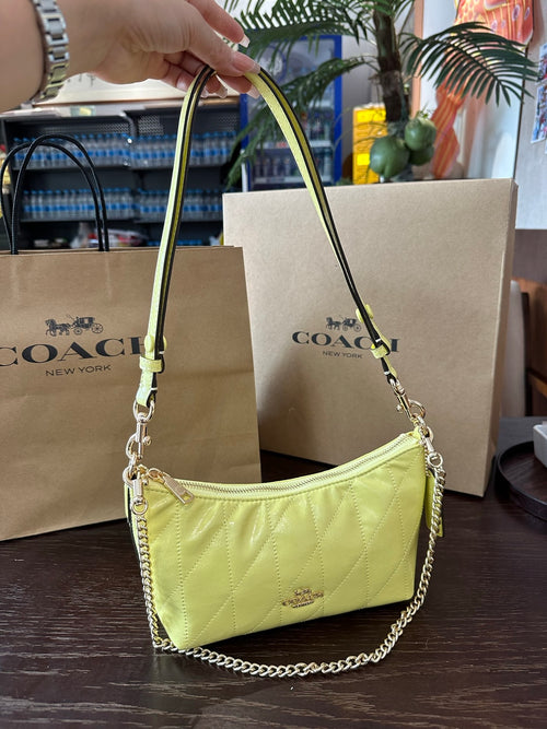 Yellow handbag with chain detail held above Coach shopping bags.