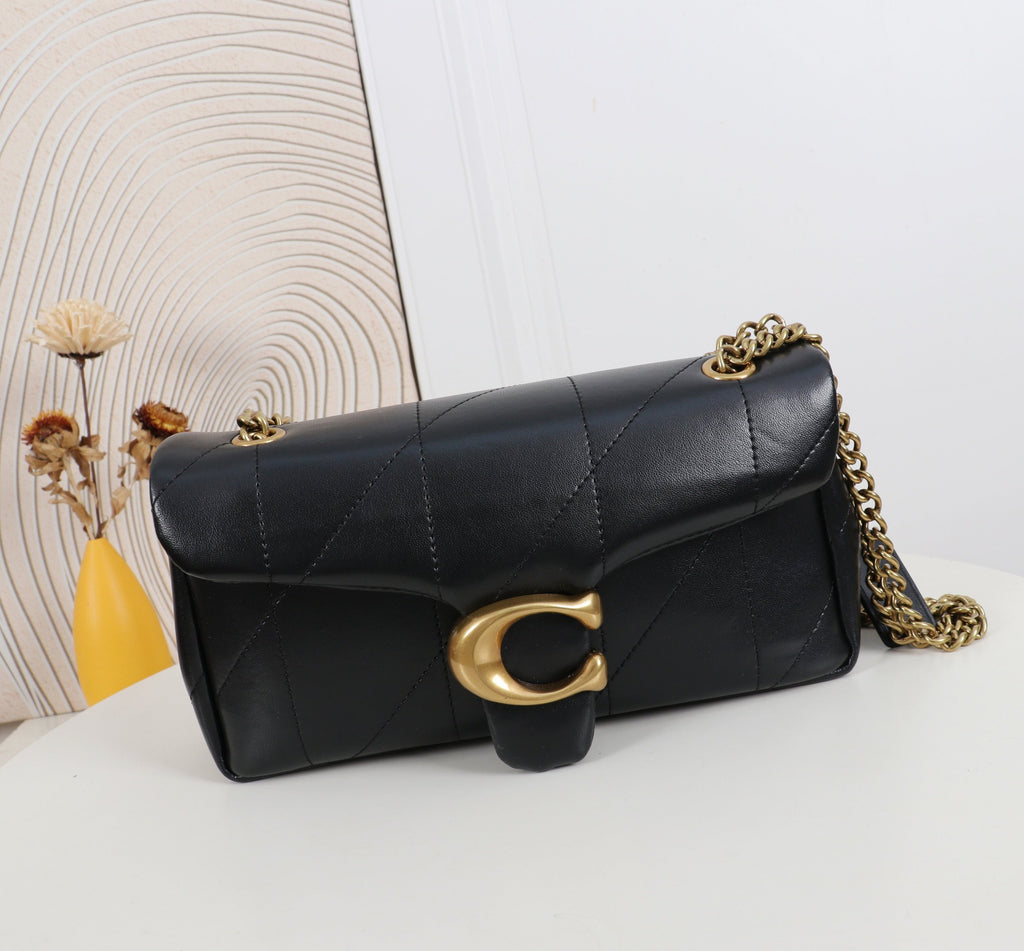 Black quilted handbag with gold chain and clasp on a white surface with a decorative wall in the background.