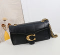 Black quilted handbag with gold chain and clasp on a white surface with a decorative wall in the background.