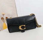 Black quilted handbag with gold chain and clasp on a white surface with a decorative wall in the background.