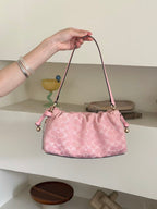 A pink Coach handbag with a signature monogram pattern is held by a person's hand in front of white shelves with decorative items.