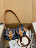 A blue and tan monogram shoulder bag with gold-tone hardware, displayed inside an open cardboard box with its dust bag and accessories.