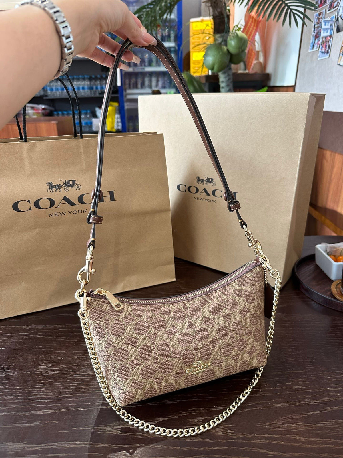 Coach handbag with a chain detail on a wooden surface with Coach bags in the background.