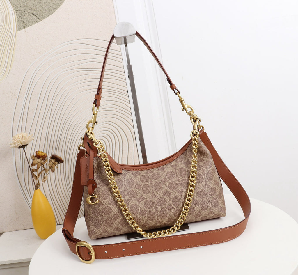 A Coach hobo shoulder bag in signature monogram canvas with brown leather trim and gold-tone chain and strap hardware, displayed on a white pedestal in a styled interior setting.