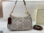A Coach signature canvas shoulder bag in light gray and beige with brown leather trim, gold-tone hardware, a matching brown leather hangtag, and an additional detachable strap placed beside it.